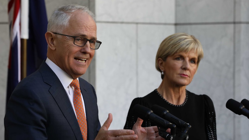 Malcolm Turnbull gestures with both hands towards the microphone. Julie Bishop stands beside him, watching the crowd.