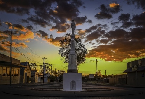 Um alto monumento de pedra fica no meio de uma pitoresca vila rural enquanto o sol se põe atrás dele.