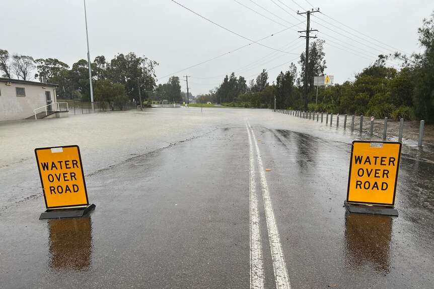 Two yellow signs saying "water over road" sit in front of flooded road 