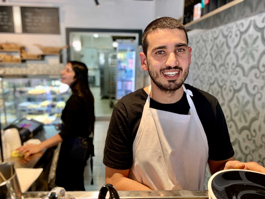 Arkan Yousif stands in his bakery holding coffee saucers.