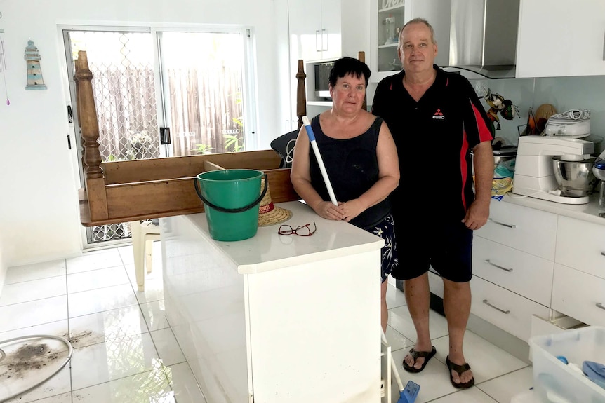 Eileen White and Ken Hamelink stand with a mop in the kitchen of their muddy townhouse.