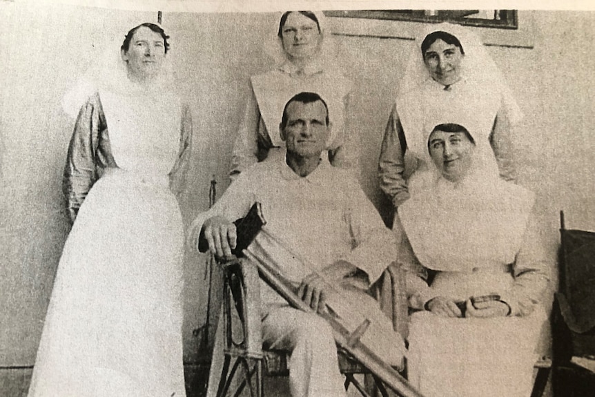 Black and white image of a veteran sitting with nurses in a hospital after having his leg amputated.