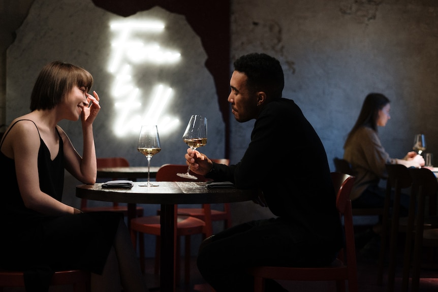 A man and a woman sit at a small table at a restaurant, drinking wine