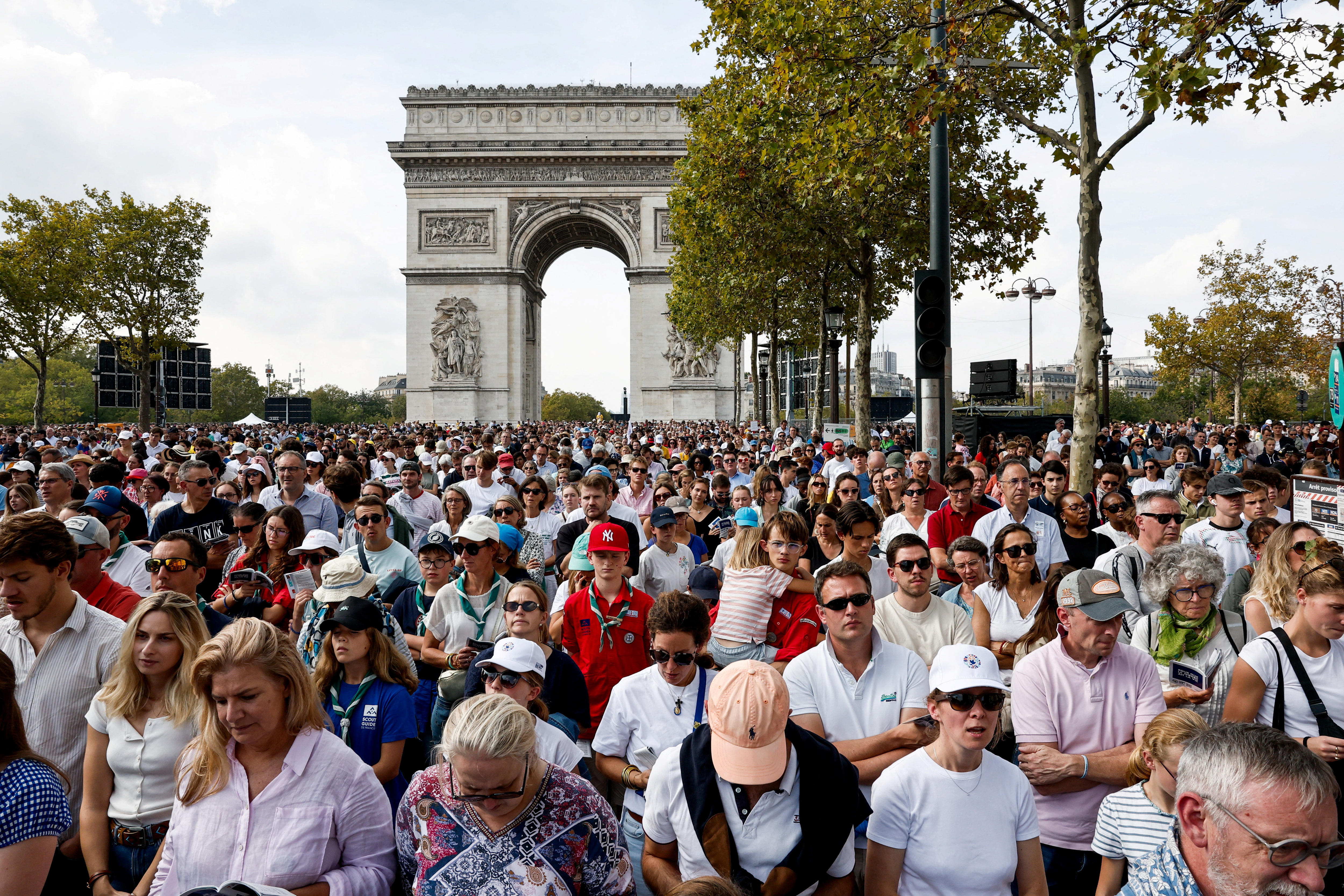 A large crowd stands and waits in front of the Arc de Triomphe.