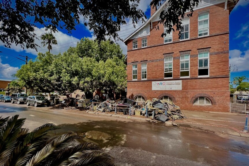 An exterior of a 3-story brick building with piles of flood trash out the front