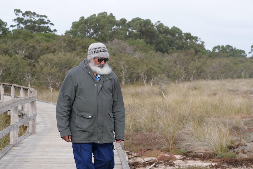 George Walley walks on boardwalk, with shrubbery and trees to his right. 