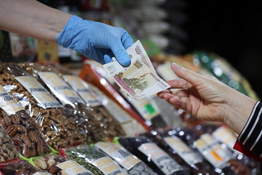 A customer hands over Russian rouble banknotes to a vendor at a market in Saint Petersburg.