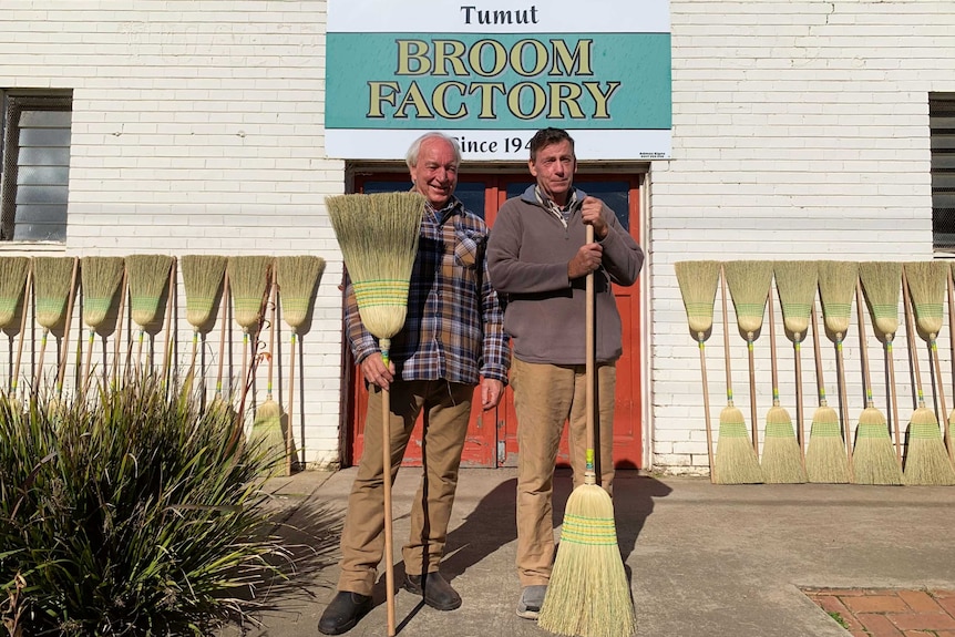 Two men stand with their brooms outside the Tumut Broom Factory.