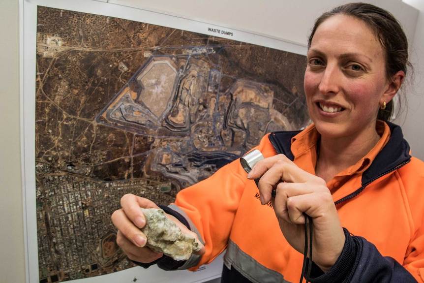 A female geologist in work clothing inspecting a rock sample.