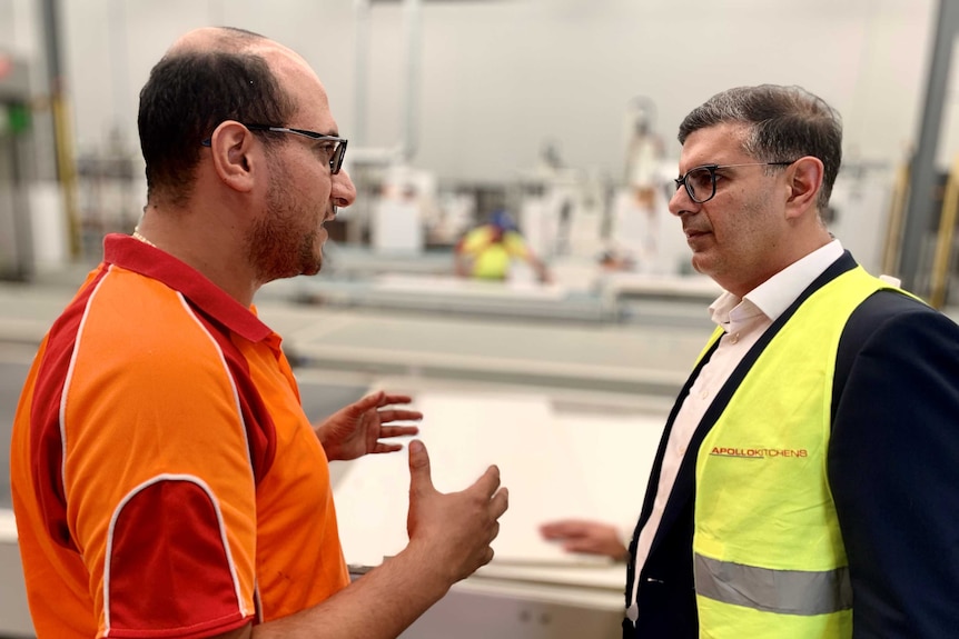 Two men face each other, speaking on a factory floor.