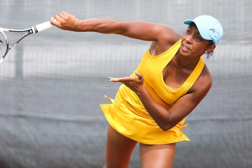 Abigail Tere-Apisah is pictured in the middle of a tennis serve pictured in a light blue cap and bright yellow dress.