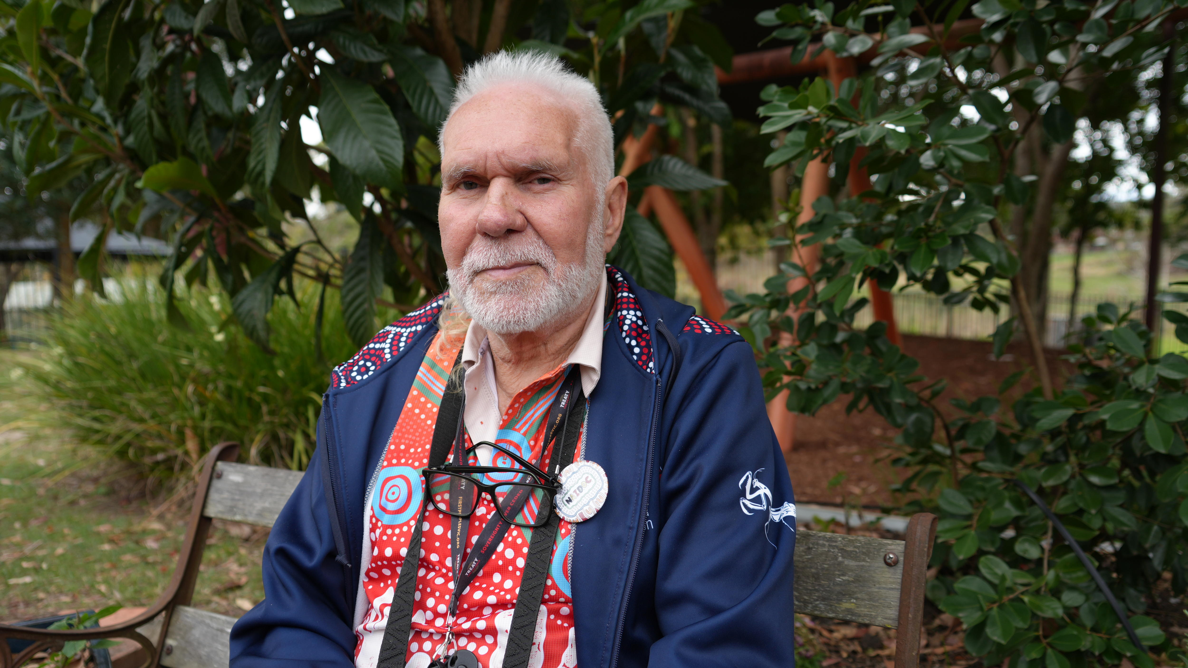 Aboriginal elder sitting in a garden with a wooden swing set behind