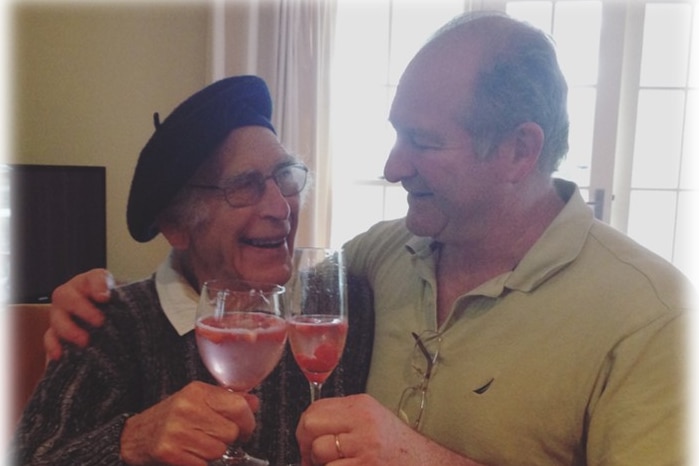 Two men with arms around each other holding glasses clinking together in cheers.