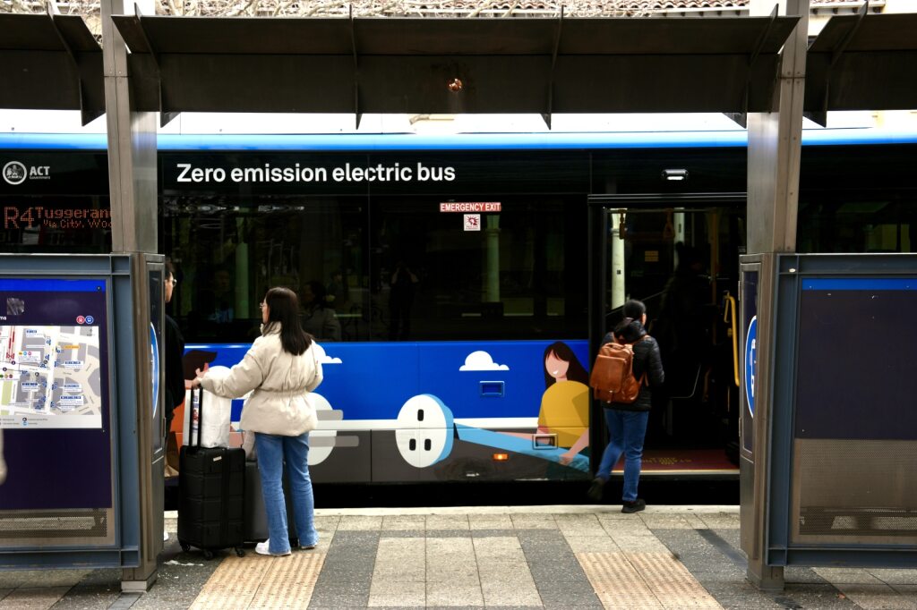 La gente se para en una parada de autobús, una mujer con una mochila sube a un autobús. 