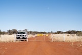 A red dirt road with a cattle gate across it, and a police truck parked on the other side.