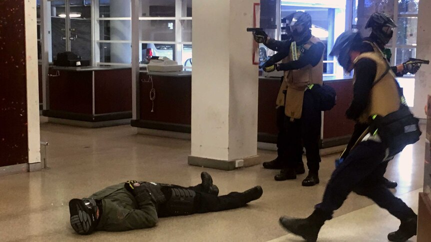 A man lays on the ground while police hold up guns.