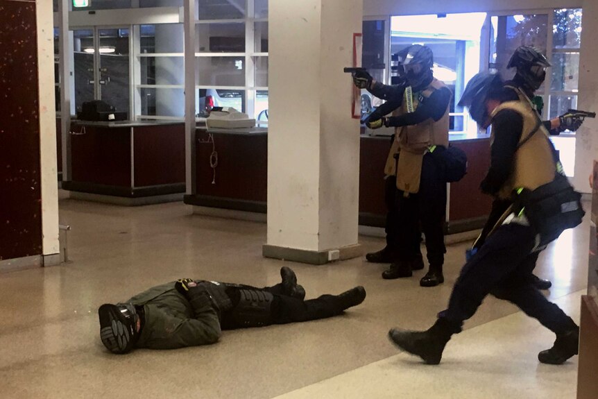A man lays on the ground while police hold up guns.