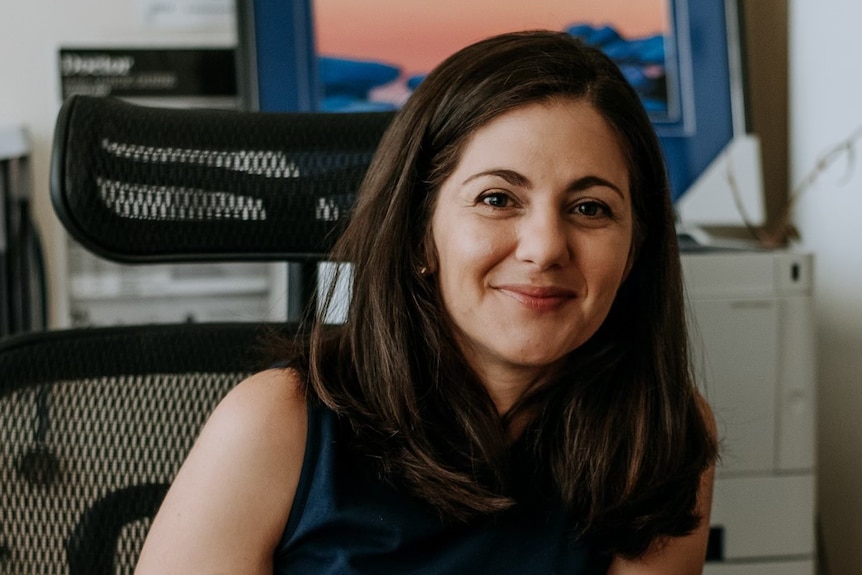 A smiling woman sits on a chair inside an office.