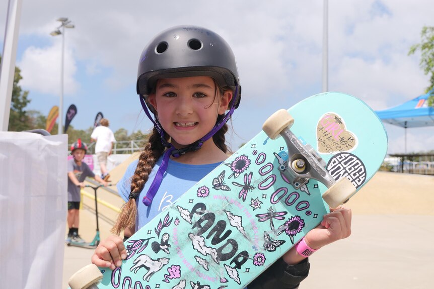 7 year old girl stands with skateboard smiling. 