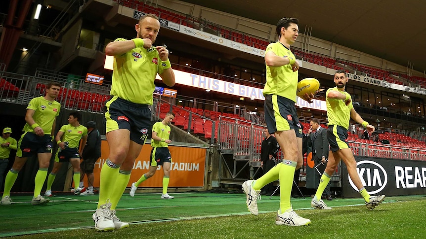 AFL umpires give signals as they step across the boundary line before a match.