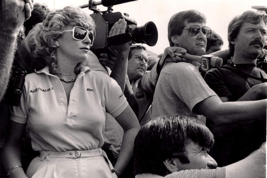 A stylishly dressed woman amid a crowd of reporters.