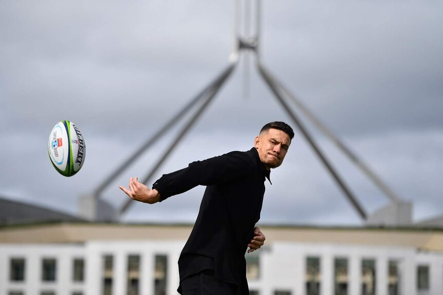 A man passes a rugby ball in front of Parliament House