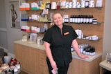 A woman in a black uniform stands smiling in front of shelves of beauty products.