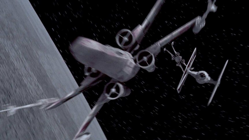 A screenshot from a Star Wars film shows an X-wing chasing a TIE fighter past the Death Star