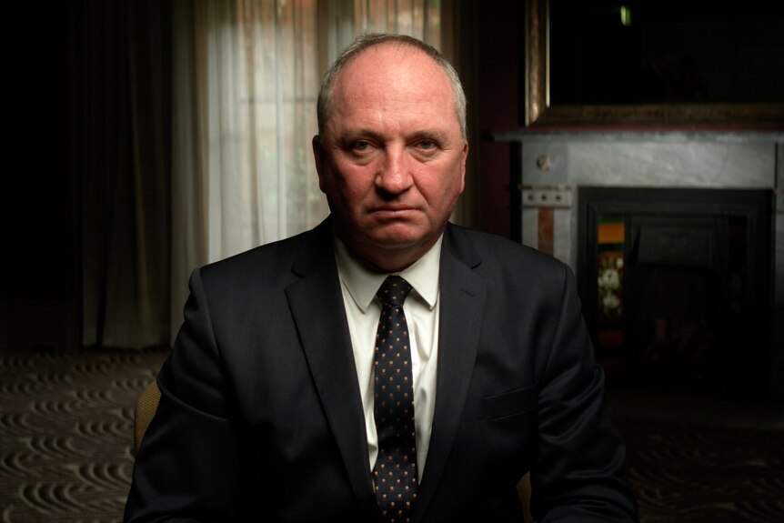 Dressed in a dark suit and tie, Barnaby Joyce sits in a room, looking into camera with a serious expression.