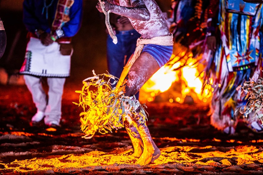 A close-up image of an Indigenous man dancing in front of a fire.
