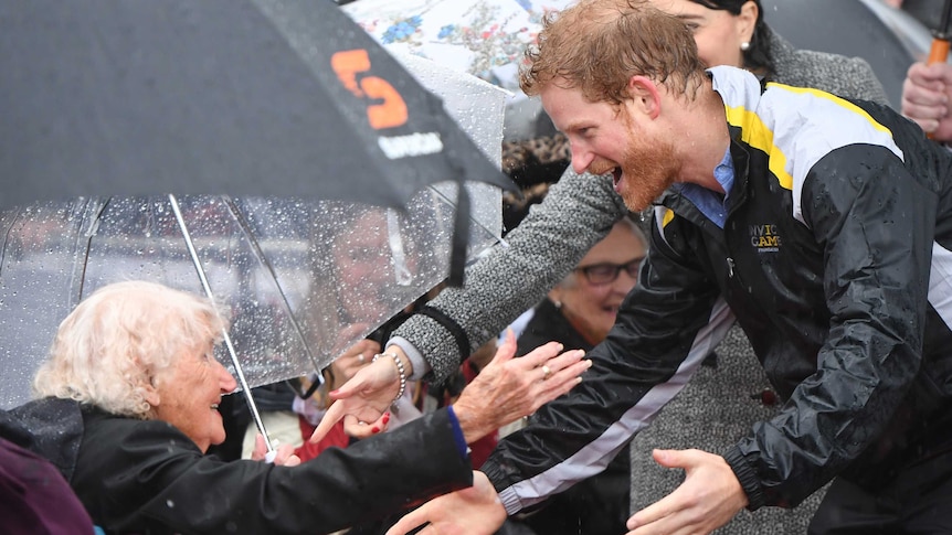 An elderly woman reaches out from a wheelchair to embrace a younger man who happily reaches out for a hugg in front of a crowd.