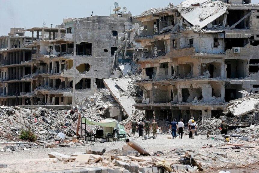 Civilians and pro-government forces walk down destroyed road in city of Damascus after regaining control from IS group.