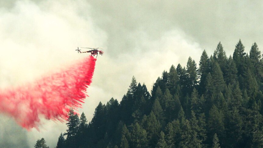 A firefighting helicopter drops red fire retardant onto an enormous forest fire in California.