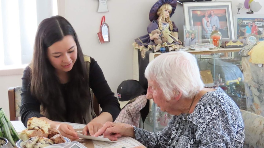 Hasinah Zainal and Peggy Muller look at old photos over scones at the kitchen table.