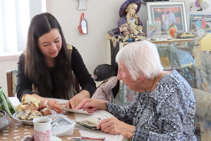 Hasinah Zainal and Peggy Muller look at old photos over scones at the kitchen table.