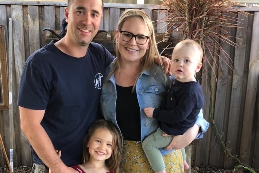 A young family pose for a photo in a backyard.