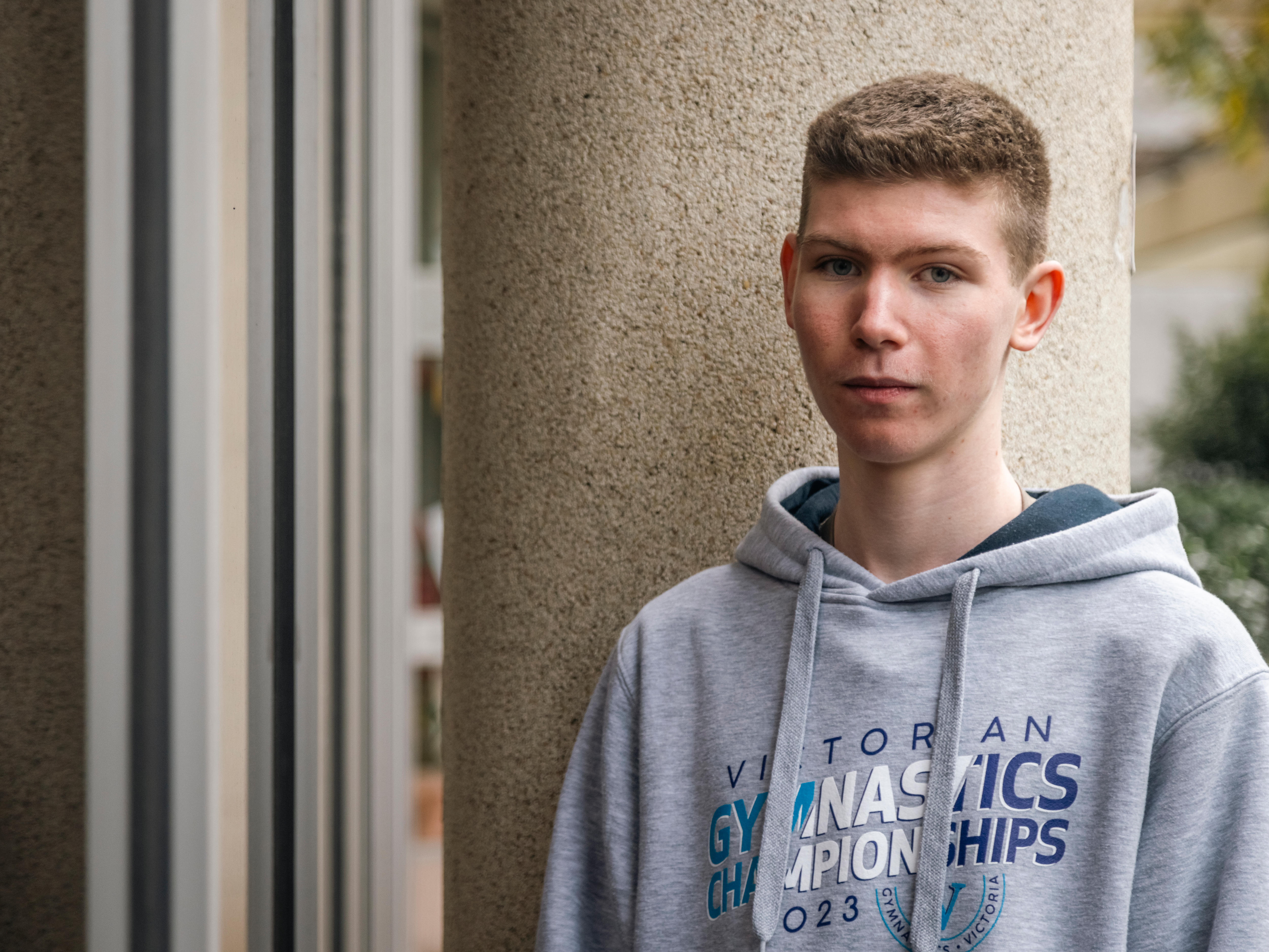 A teenage boy with short hair wearing a grey hoodie gazes into the camera.