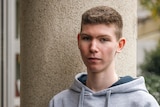 A teenage boy with short hair wearing a grey hoodie gazes into the camera.