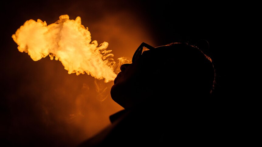 A silhouette of a person vaping with an orange light behind the vapour cloud. 