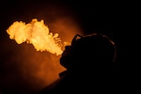 A silhouette of a person vaping with an orange light behind the vapour cloud. 