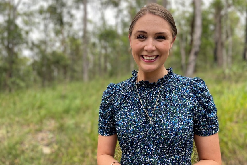 Ms Scanlon wearing a blue and green dress standing in the forest smiling. 