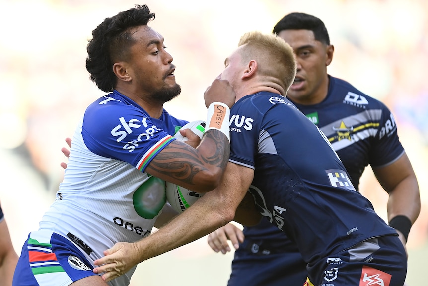 A Warriors NRL player carries the ball as he is met in defence by a North Queensland Cowboys opponent.
