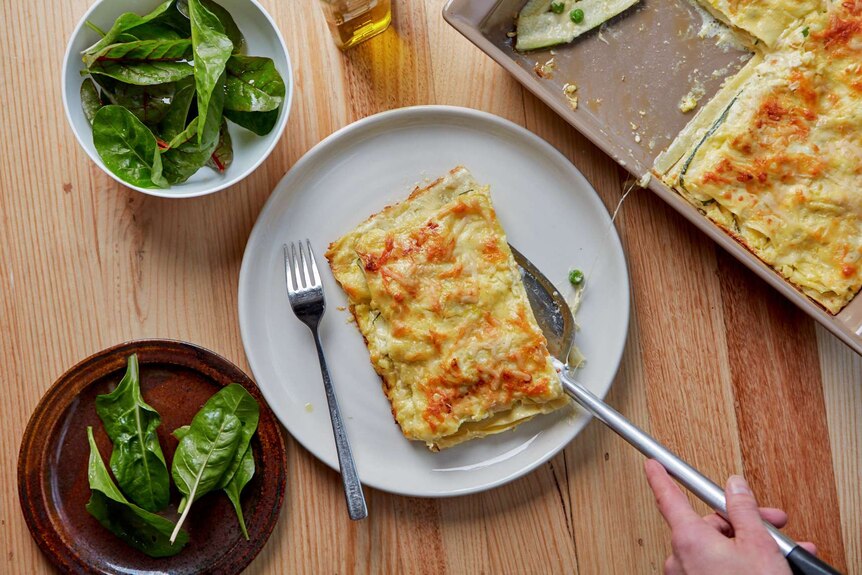 A serving of vegetarian lasagne on a plate with a leafy side salad and the remaining lasagne nearby, a family dinner.