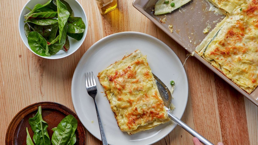 A serving of vegetarian lasagne on a plate with a leafy side salad and the remaining lasagne nearby, a family dinner.