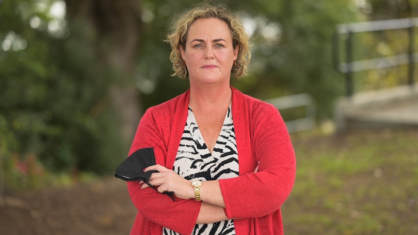 A woman stands crossed arms, staring at the camera.