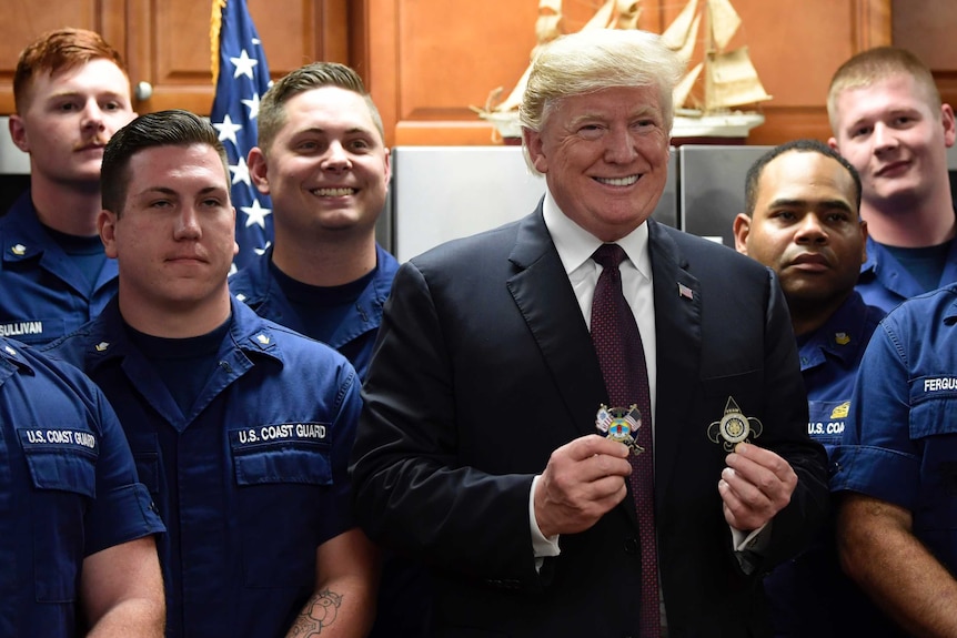 men in uniform and one in a suit pose for a photo with the man in a suit holding medals