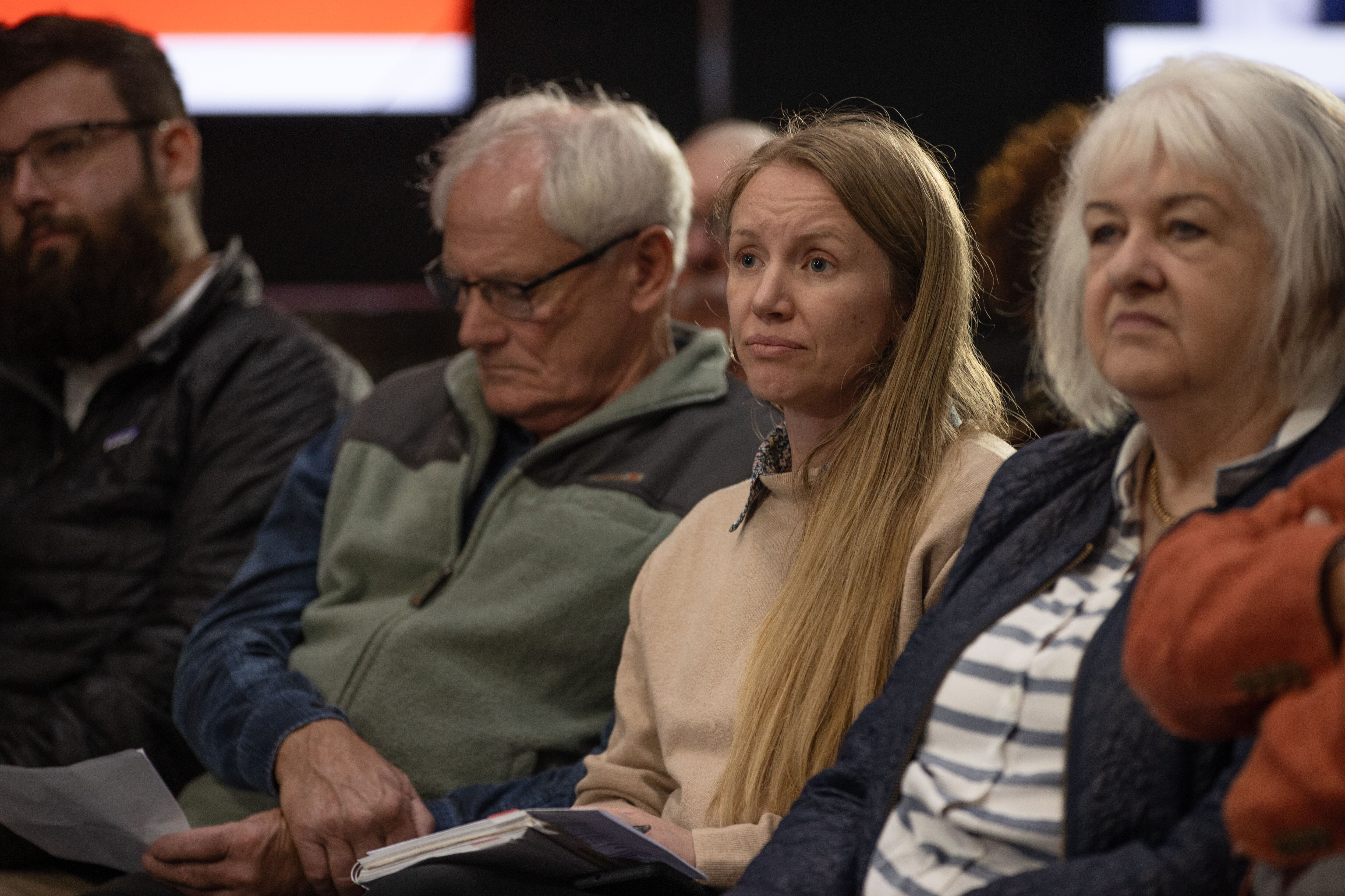 A woman with blonde hair listening to a panel whilst seated in an audience.