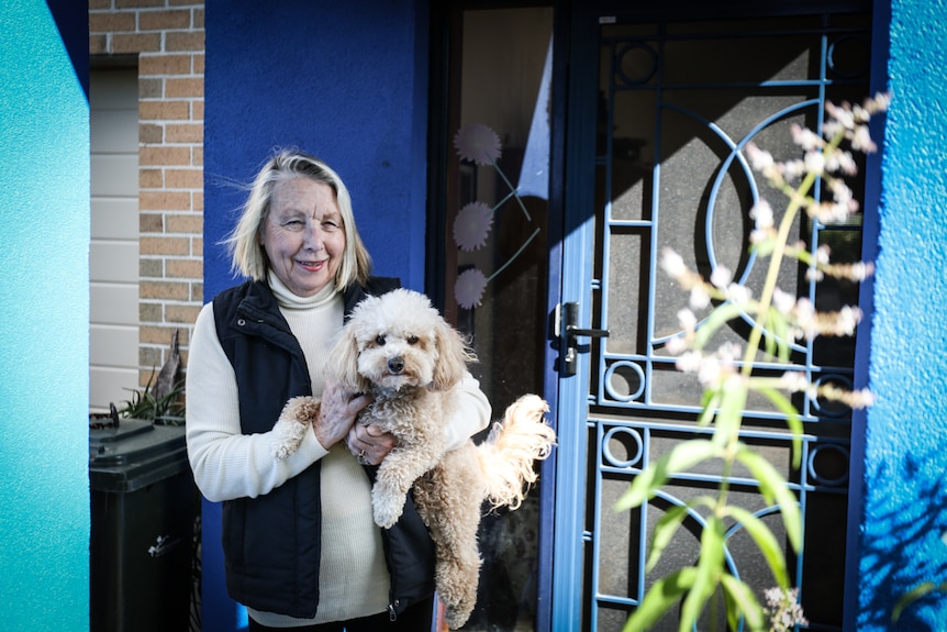Margaret Naughton holding her dog Frida Sparkles at her front door entrance.