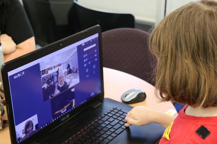 A girl watches her classmate on a laptop.