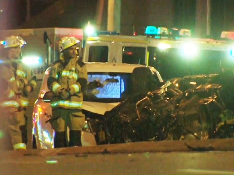 Fire crews standing around the wreckage of a car with fire truck in background.